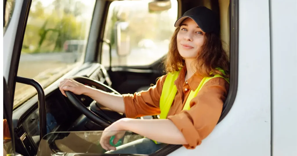 Woman truck driver in a safety vest and cap sitting in the cab of a commercial truck