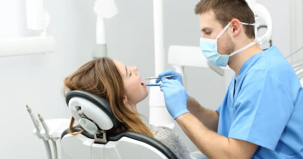 Dentist in blue scrubs and mask examining a female patient in a dental chair