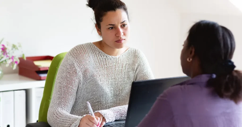 Woman meeting with a caseworker at a desk, taking notes during a social services intake appointment