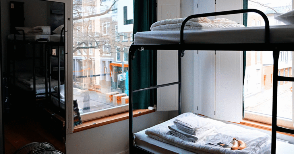 Bunk beds with folded linens in a shared room with large windows overlooking a city street