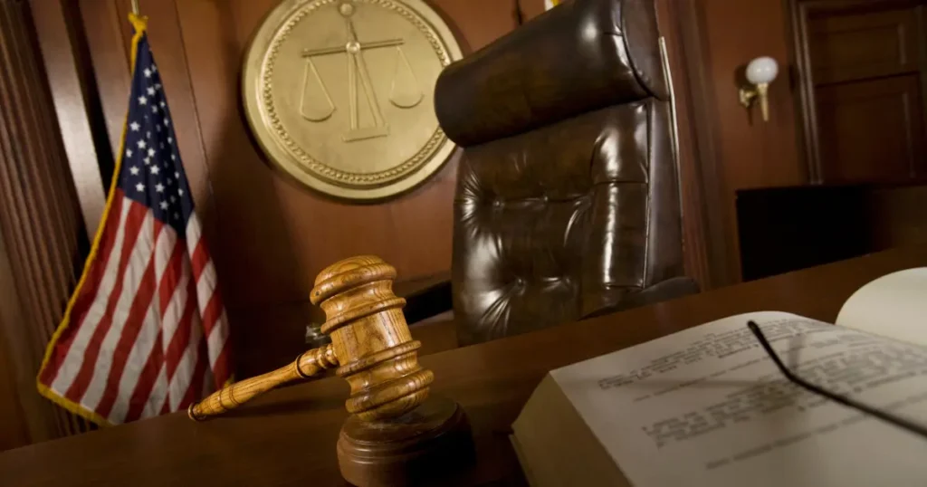 Judge's gavel on a courtroom bench with scales of justice emblem and American flag in the background