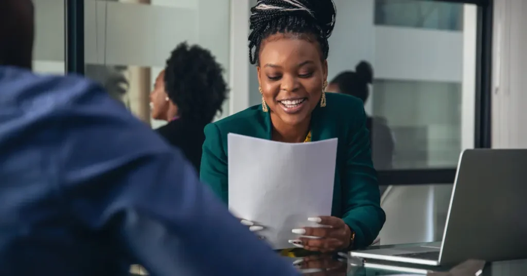 Black female hiring manager smiling while reviewing a resume document during a job interview