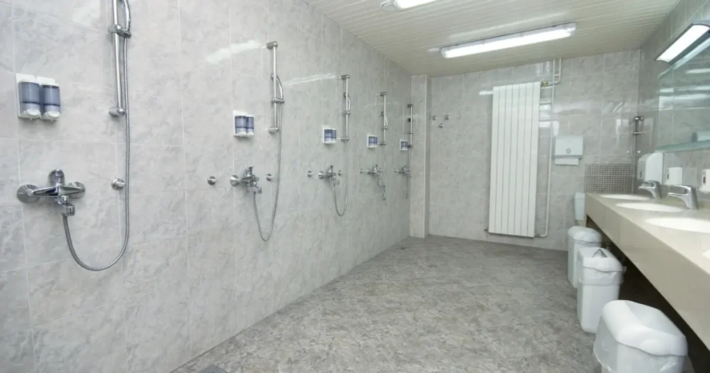 Basic public shower facility with multiple shower heads and soap dispensers along a tiled wall