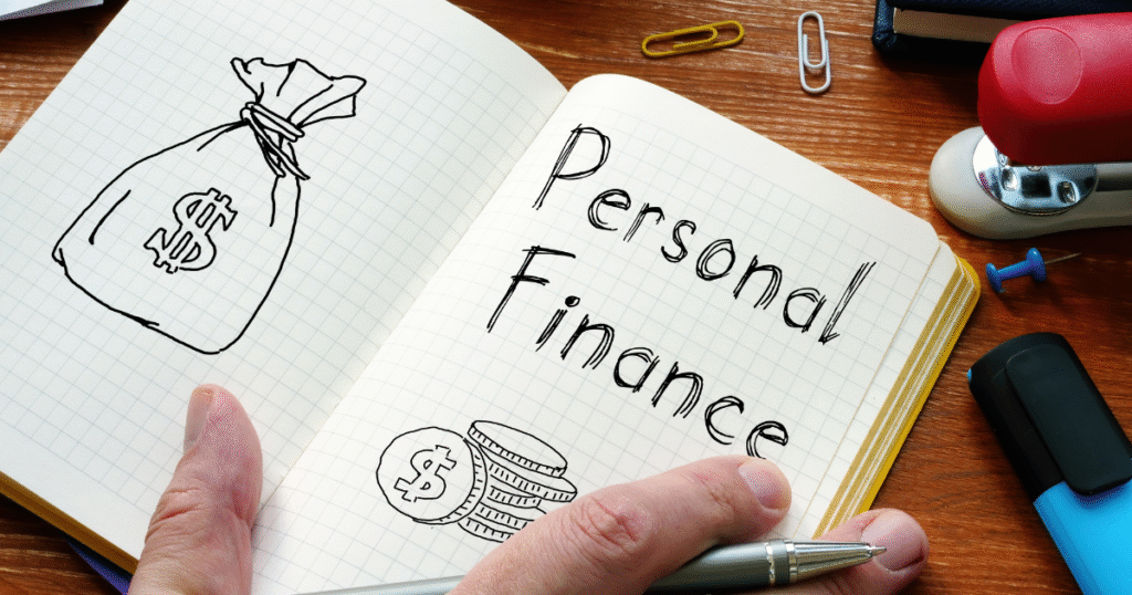 Hands holding a notebook with "Personal Finance" written alongside drawings of a money bag and coins