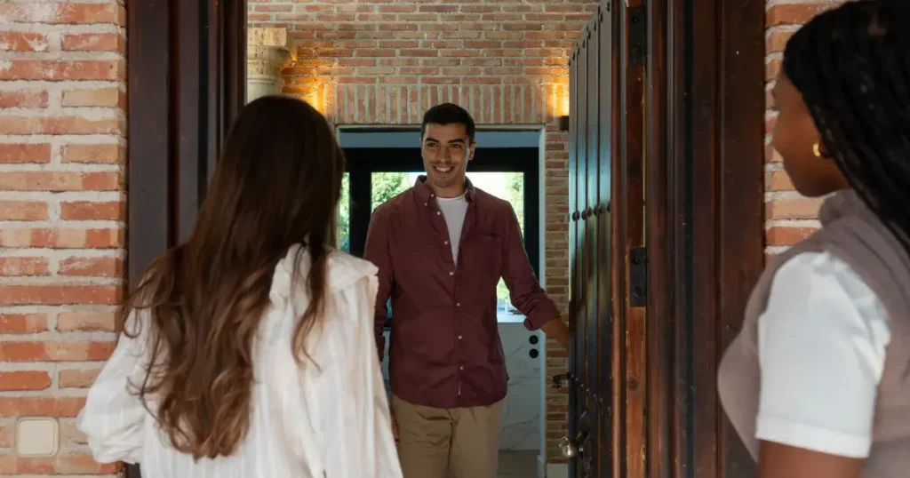 Man welcoming two people at the front door of a brick house