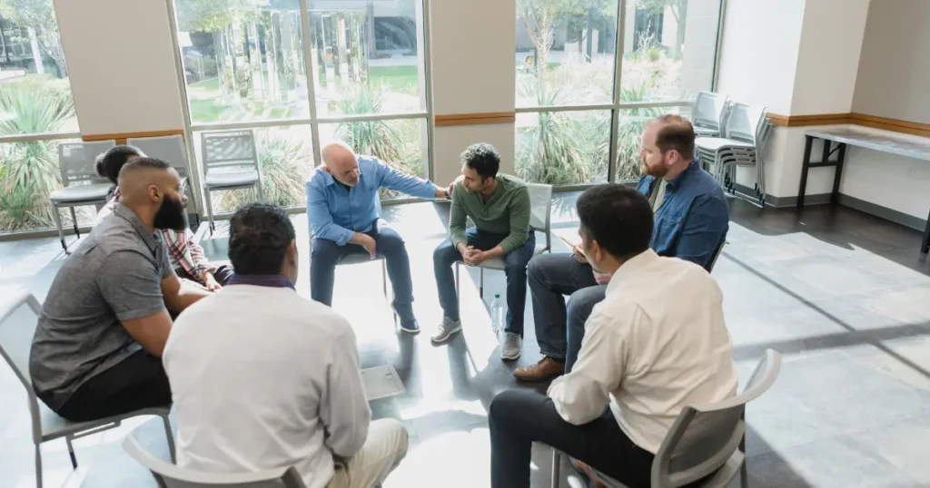 Diverse group of men sitting in a circle during a group therapy or support program session