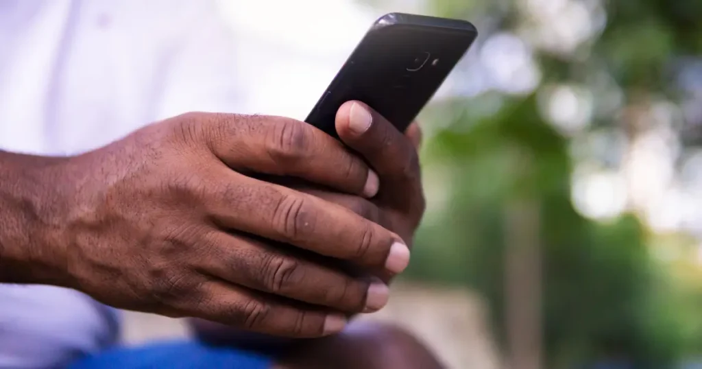 Close-up of a Black man's hands holding a smartphone outdoors