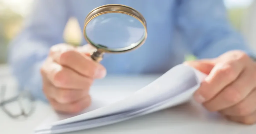 Man reviewing documents with magnifying glass to identify legitimate grants and avoid scams