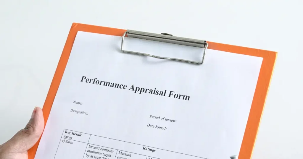 Hand holding a clipboard with a performance appraisal form showing key result areas and ratings