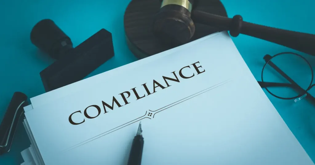 Compliance document with a gavel, rubber stamp, pen, and glasses on a teal surface